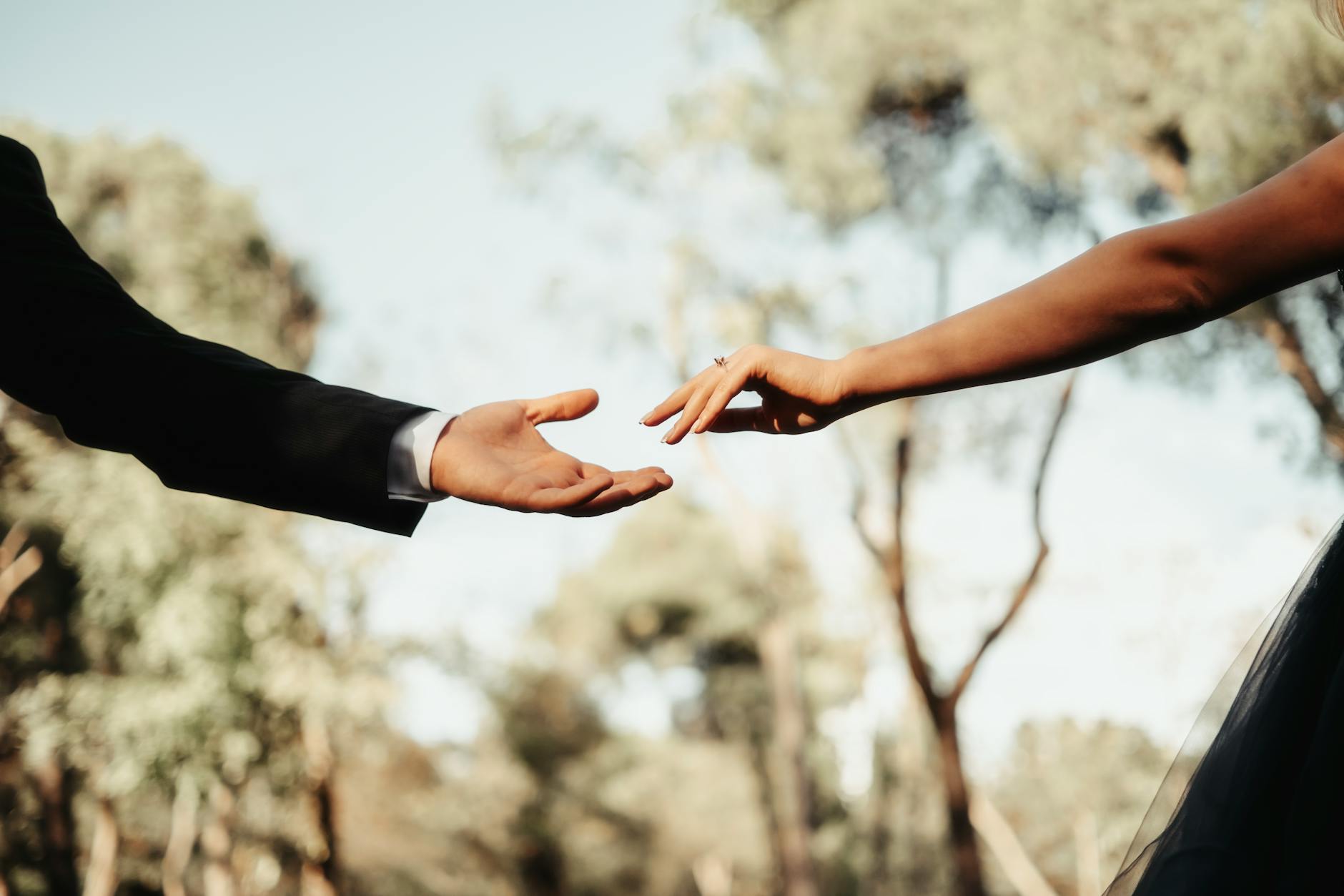 Close-up of a couple's hands reaching towards each other outdoors, evoking romance and connection. - rekindle marriage connection
