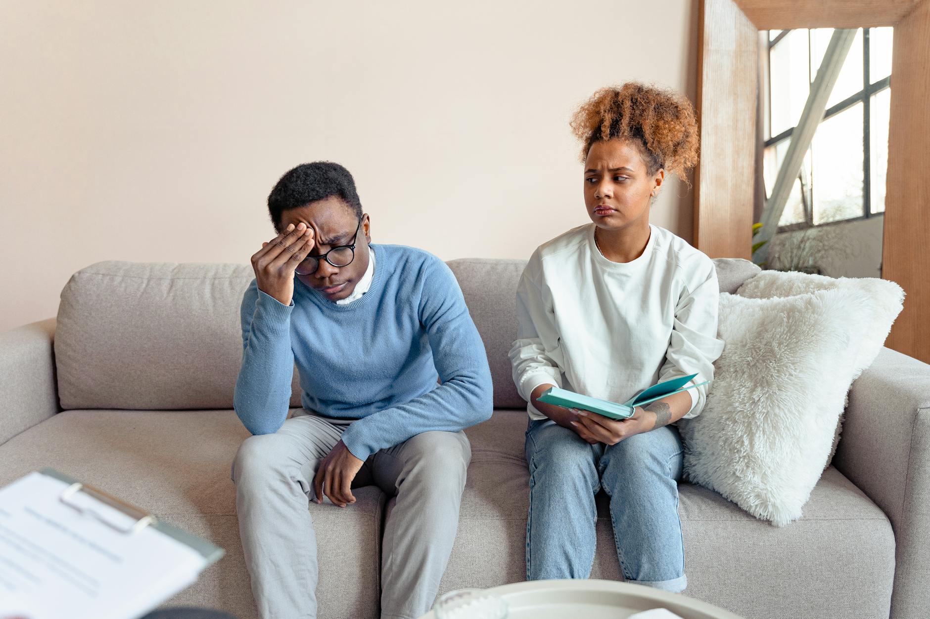 Two people sitting on a sofa indoors, engaged in a serious discussion during a therapy session. - relationship boredom therapy