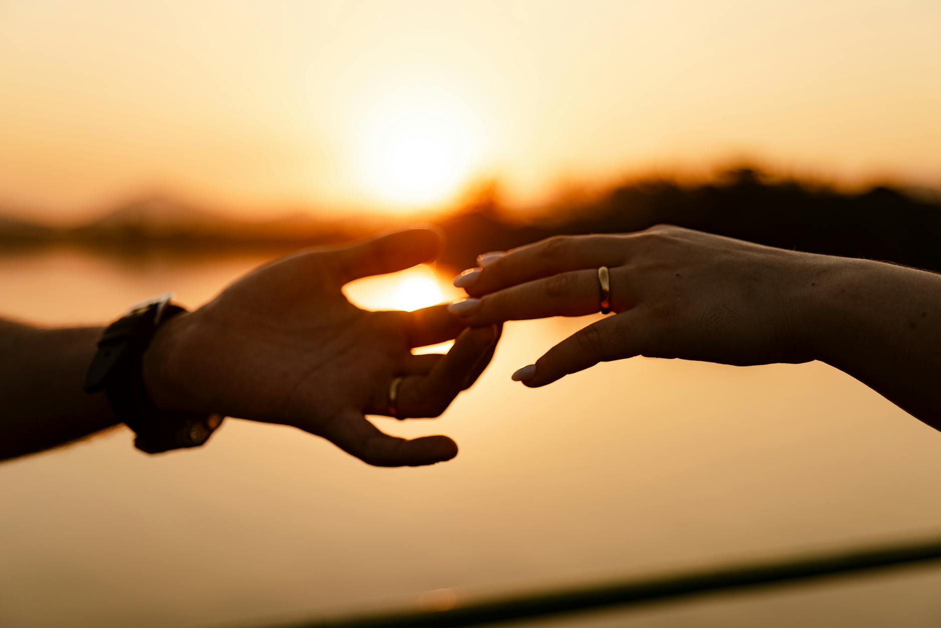 Silhouette of hands touching against a warm sunset, highlighting intimate connection. - relationship check in