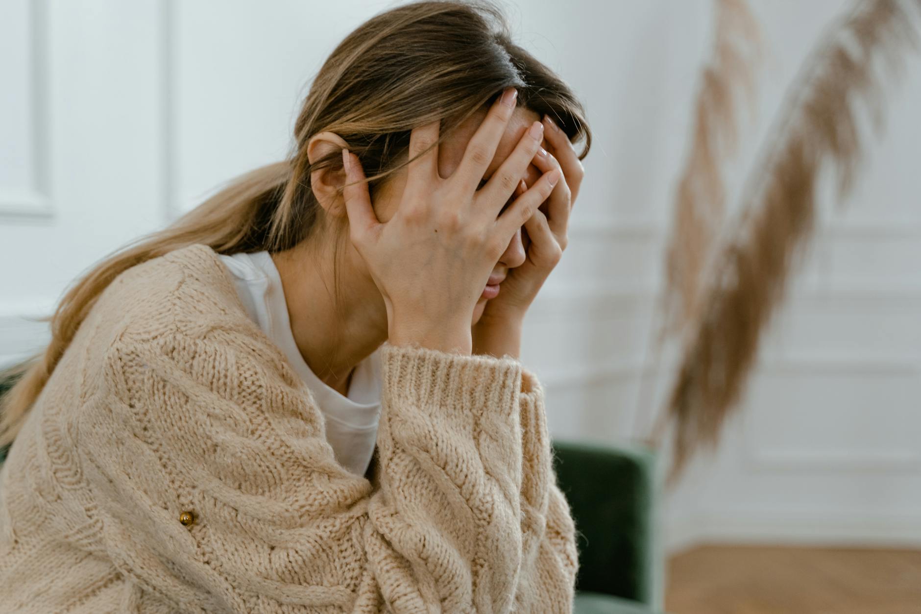 A woman sitting indoors covering her face in frustration, depicting stress and mental health challenges. - seasonal depression treatment