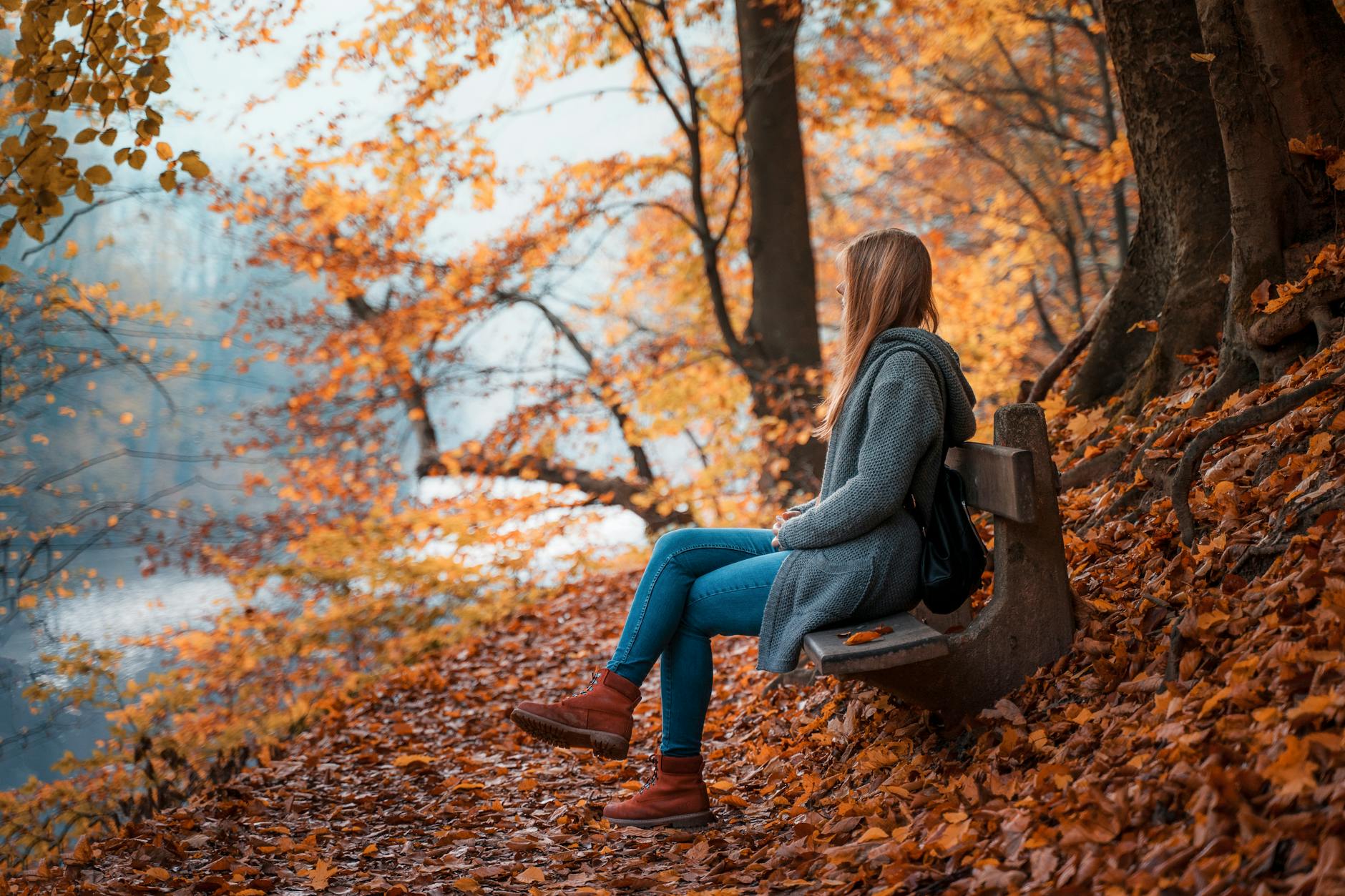 A woman sitting on a bench in a vibrant autumn forest, enjoying nature's colors. - seasonal mood boost
