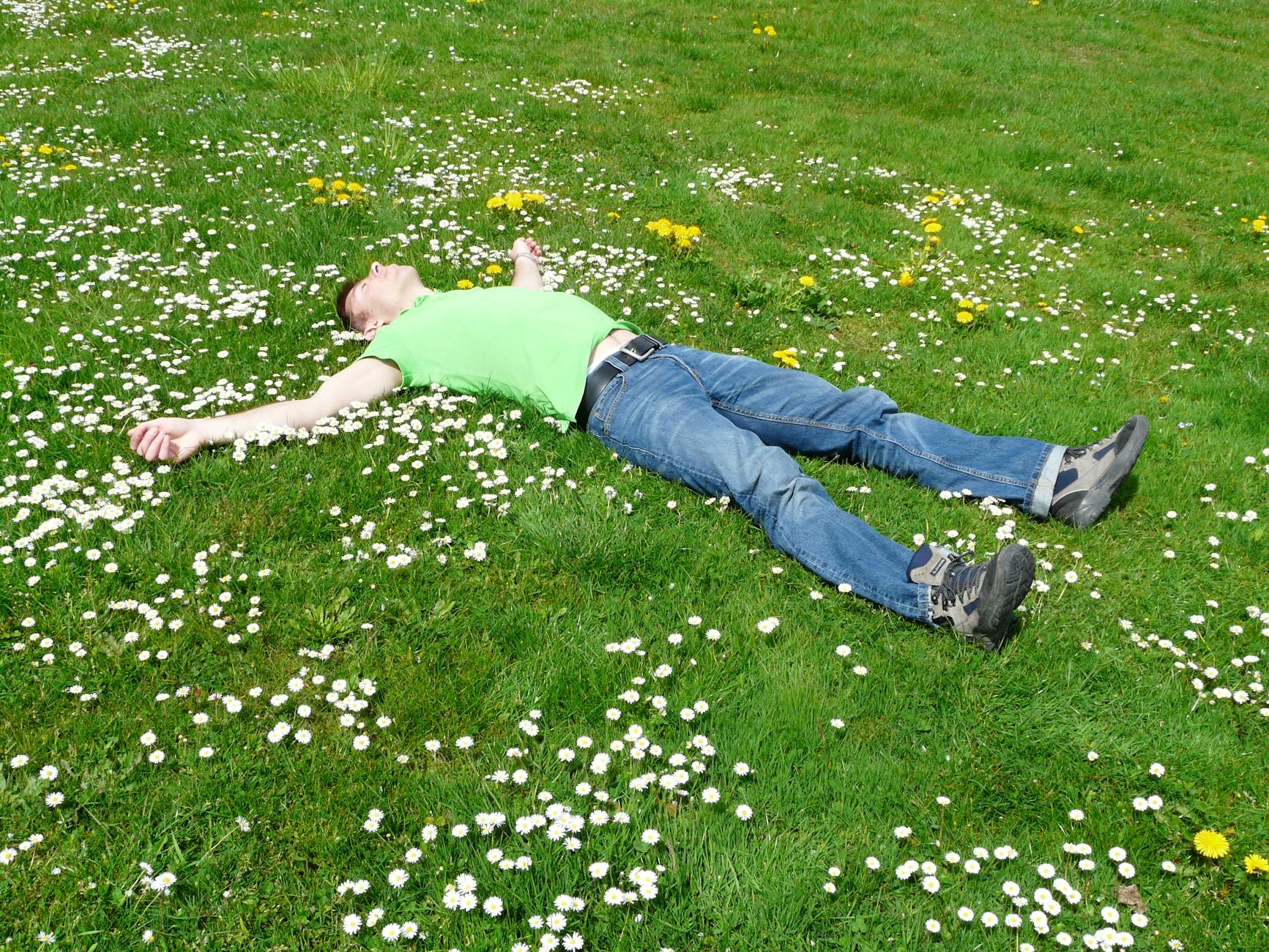 A man lies peacefully in a flowered meadow, embodying relaxation and summer joy. - spring fatigue remedies
