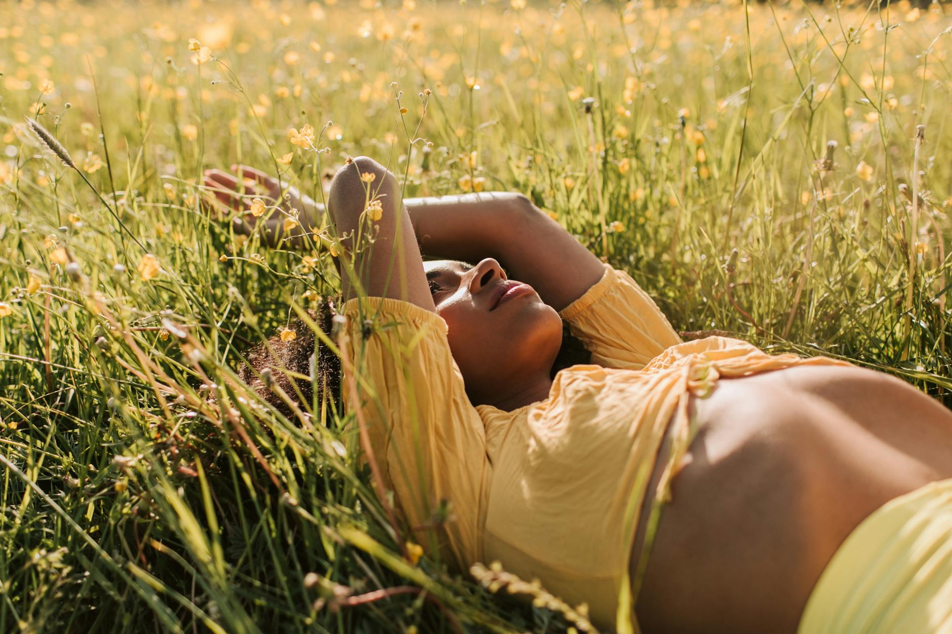 A woman in yellow enjoys a peaceful moment lying in a sunlit field of wildflowers. - spring fatigue remedies