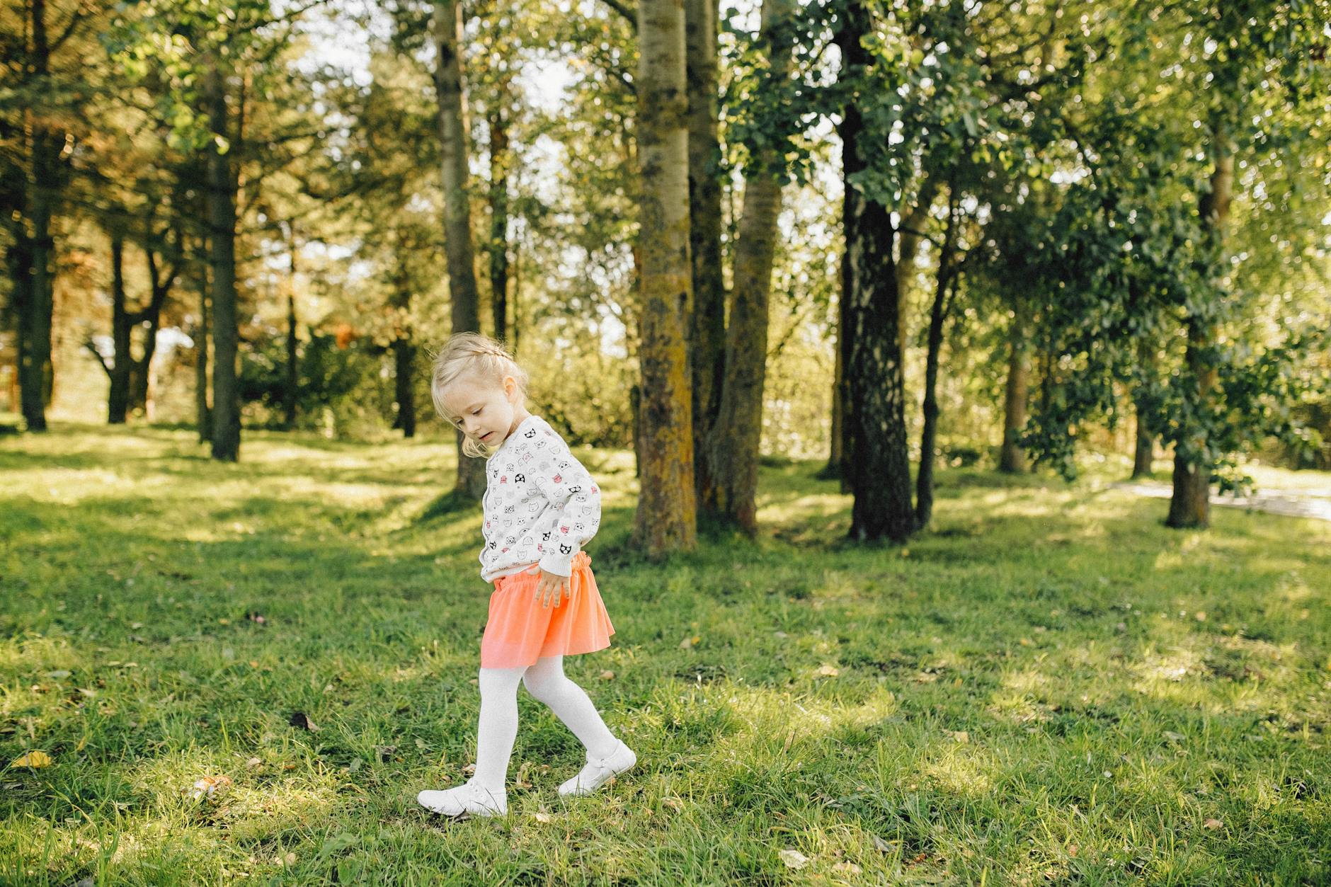 A young girl happily plays in a sunlit forest, surrounded by lush greenery and trees. - spring outdoor safety