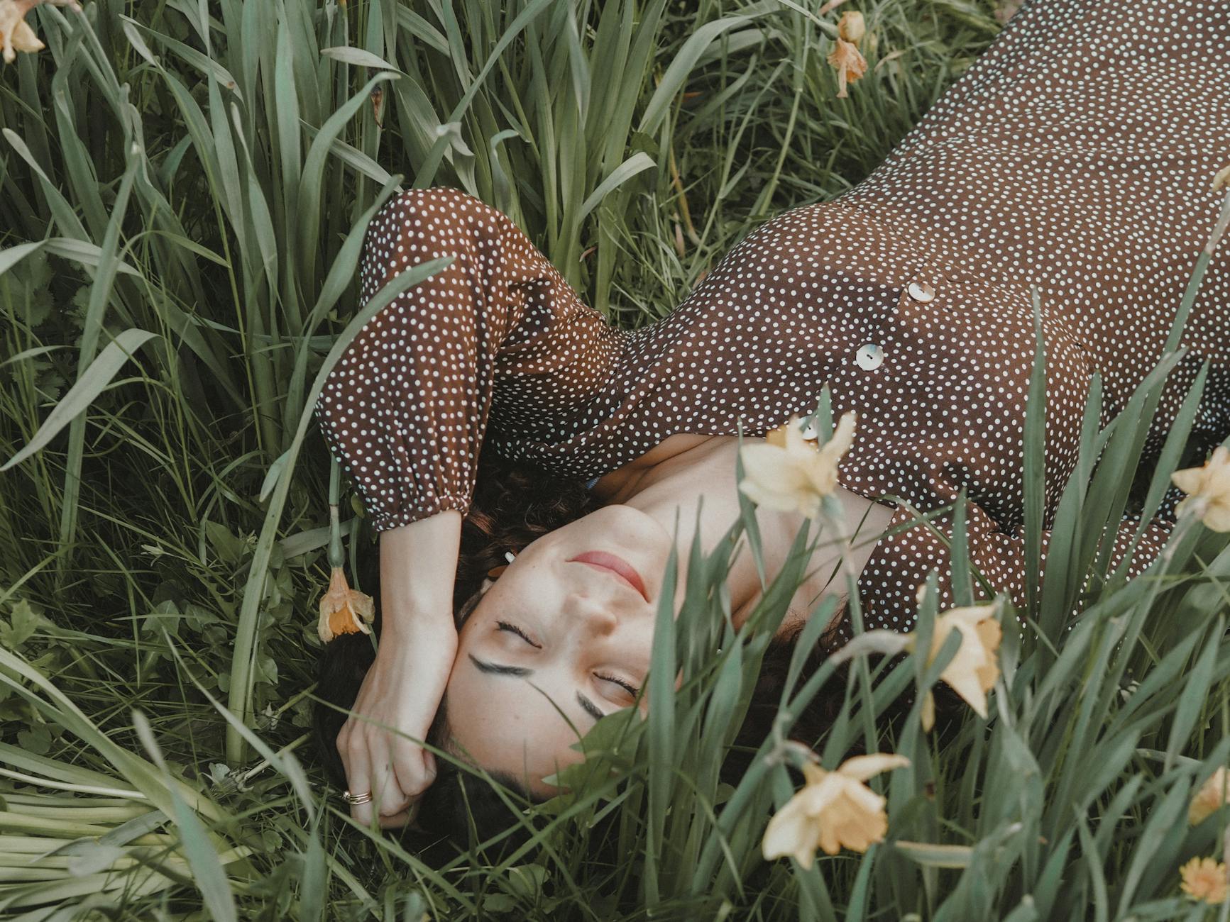 From above of positive female in stylish dress lying on ground among flowers in nature in daytime - spring stress management