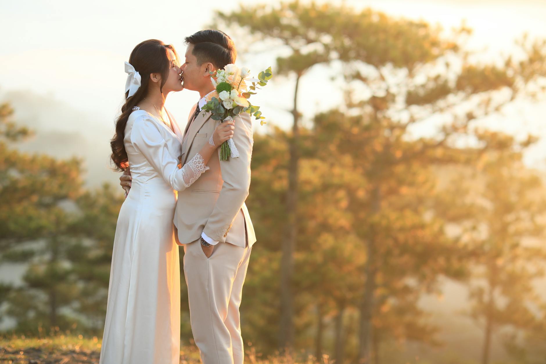 A bride and groom share a romantic kiss during their outdoor wedding at sunset. - spring wedding survival