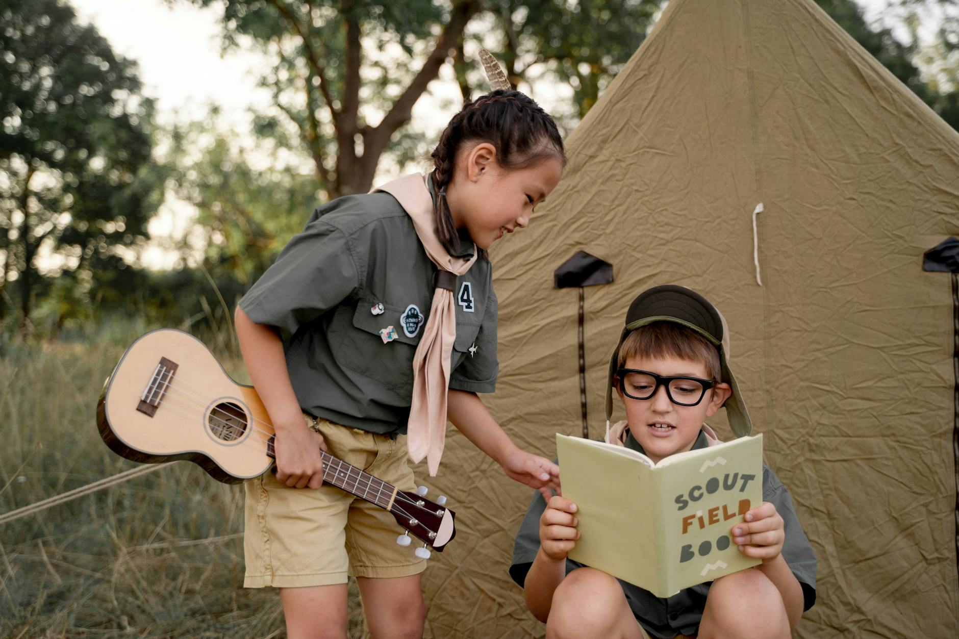 Kids in scout uniforms enjoying a camping experience with a guitar and scout field book outdoors. - summer camp fears