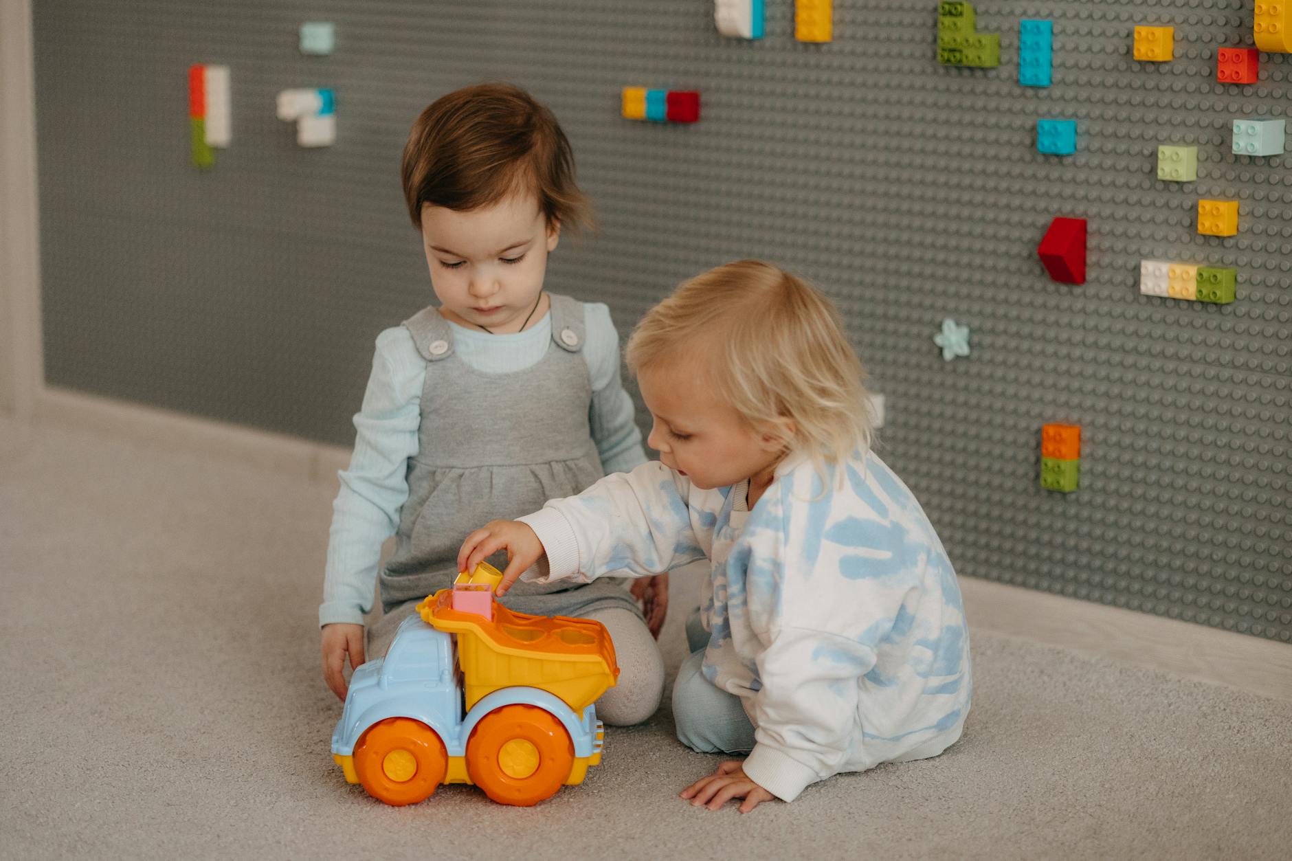 Two young children playing with a toy truck in a cozy indoor setting, exploring together. - teaching toddlers sharing