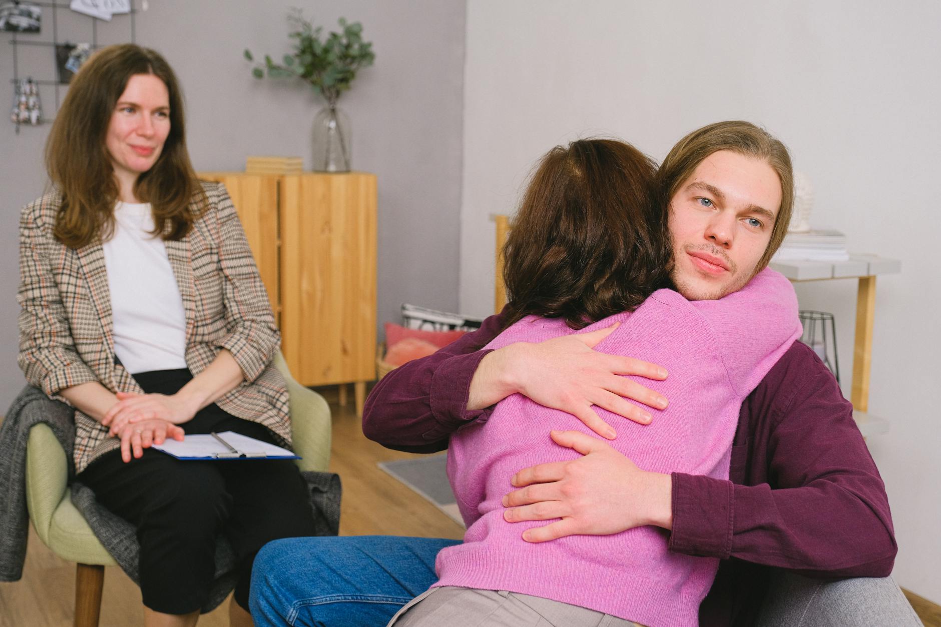 Calm couple in casual clothes sitting and embracing during session with psychologist in light room with wooden furniture - therapist for relationship anxiety