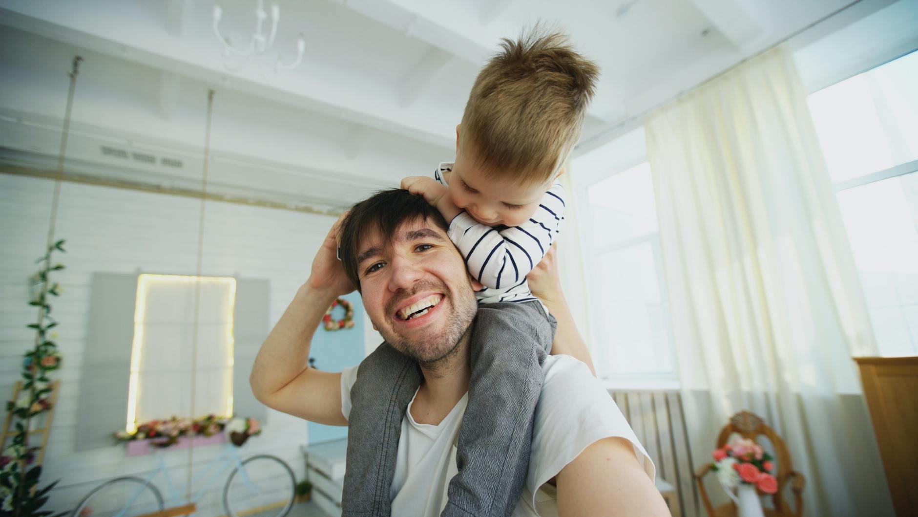 Smiling father giving piggyback ride to his young son in a bright, cheerful room. - toddler self care