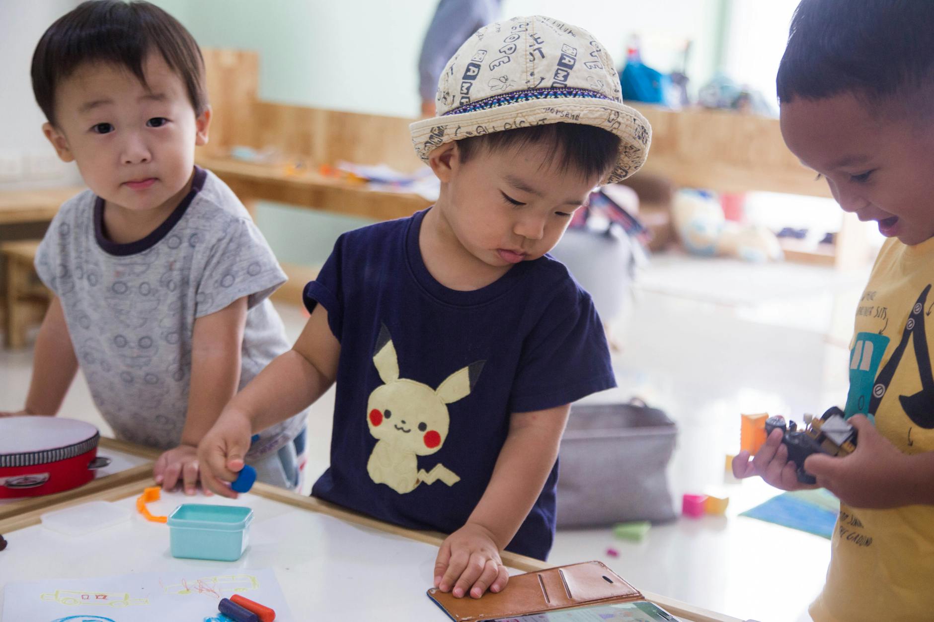 Three young children playing creatively indoors with toys and art supplies. - toddler sharing