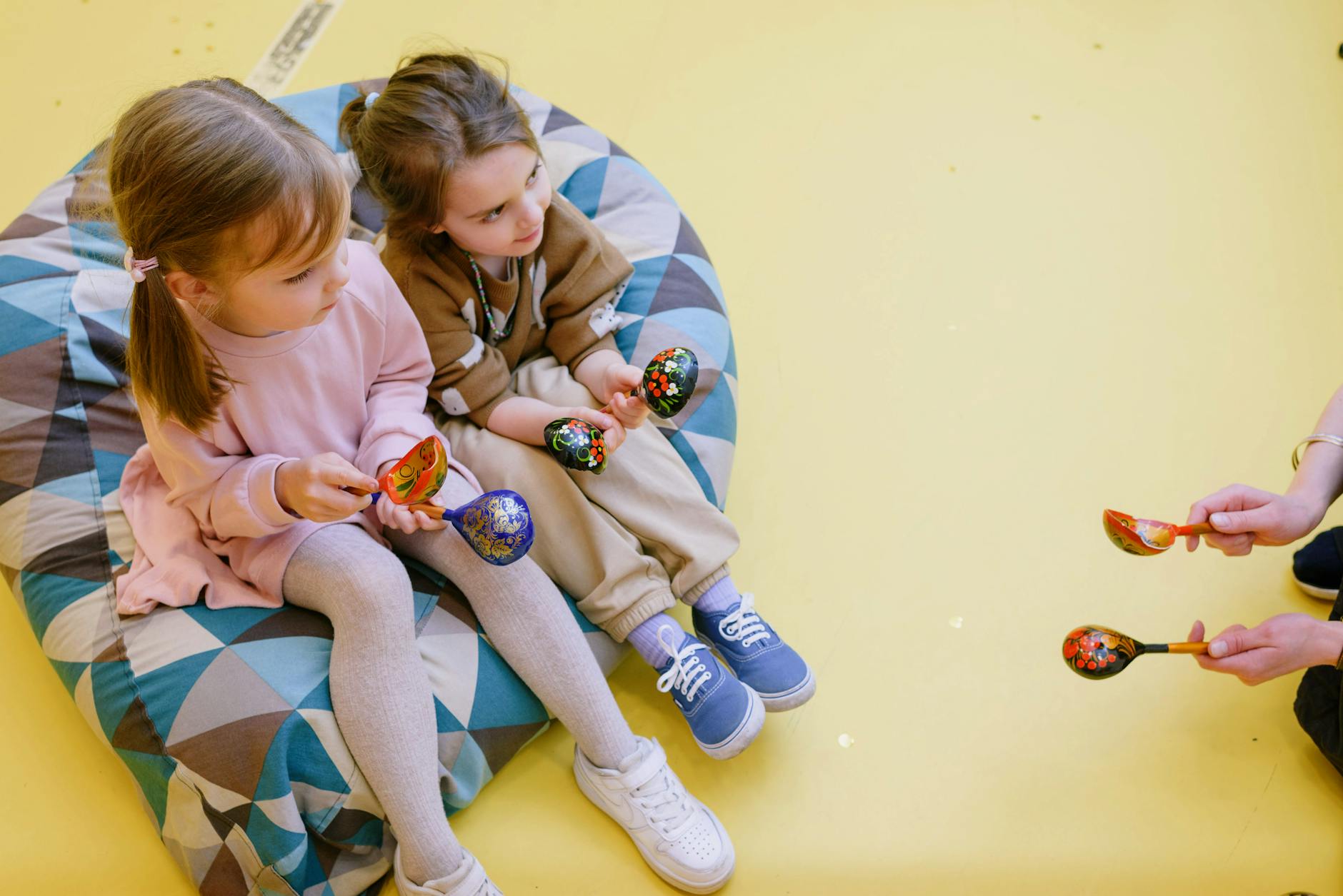 Two children joyfully play maracas indoors, capturing youthful fun on a vibrant beanbag. - toddler sharing