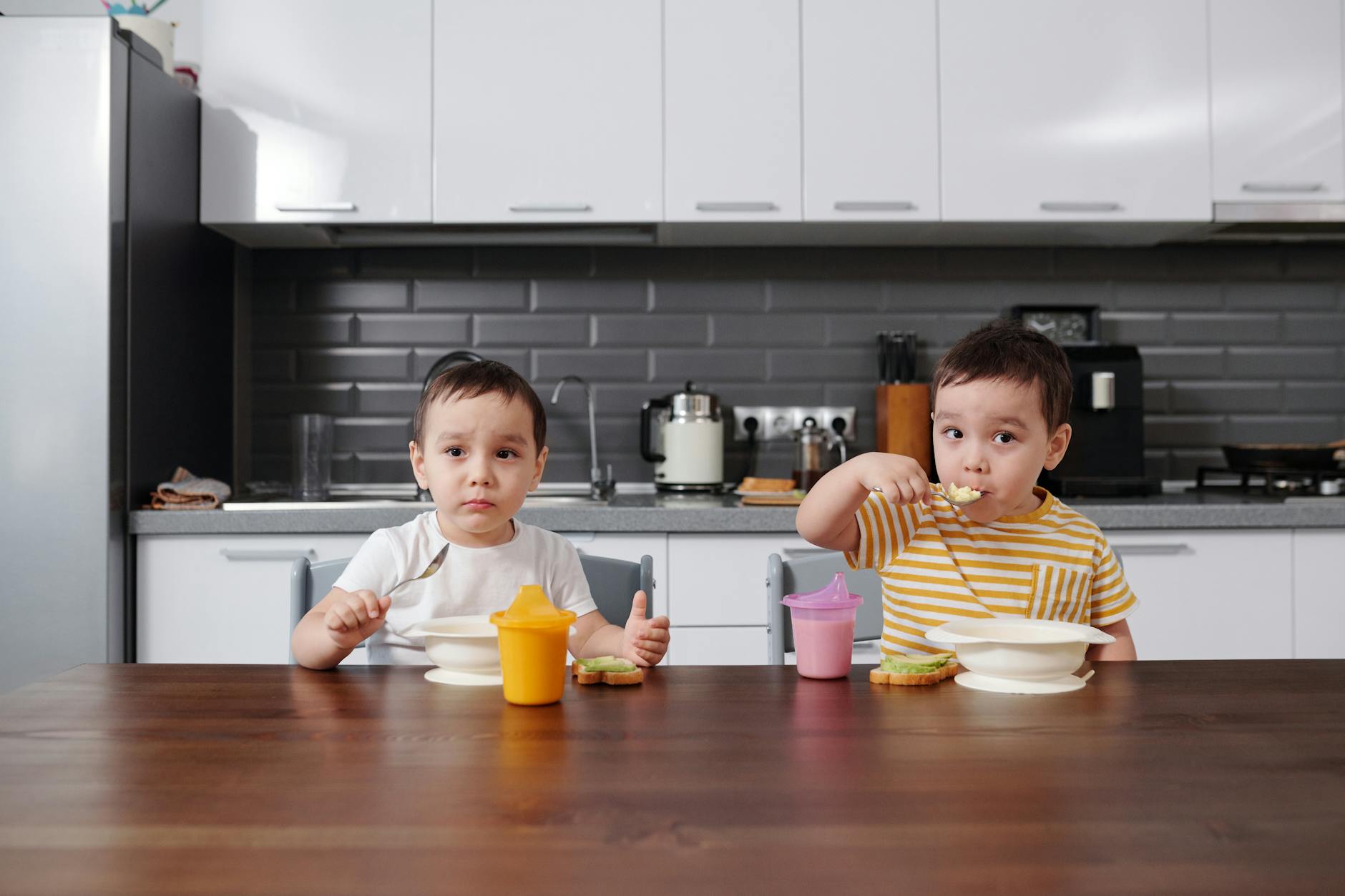 Two young boys eating breakfast at a kitchen table, enjoying food and drinks. - toddler sharing