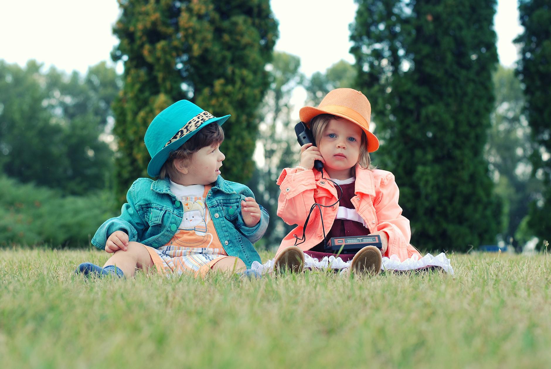 Two toddlers in colorful outfits enjoying playtime with walkie talkies in a sunny park setting. - toddler sleepaway camp