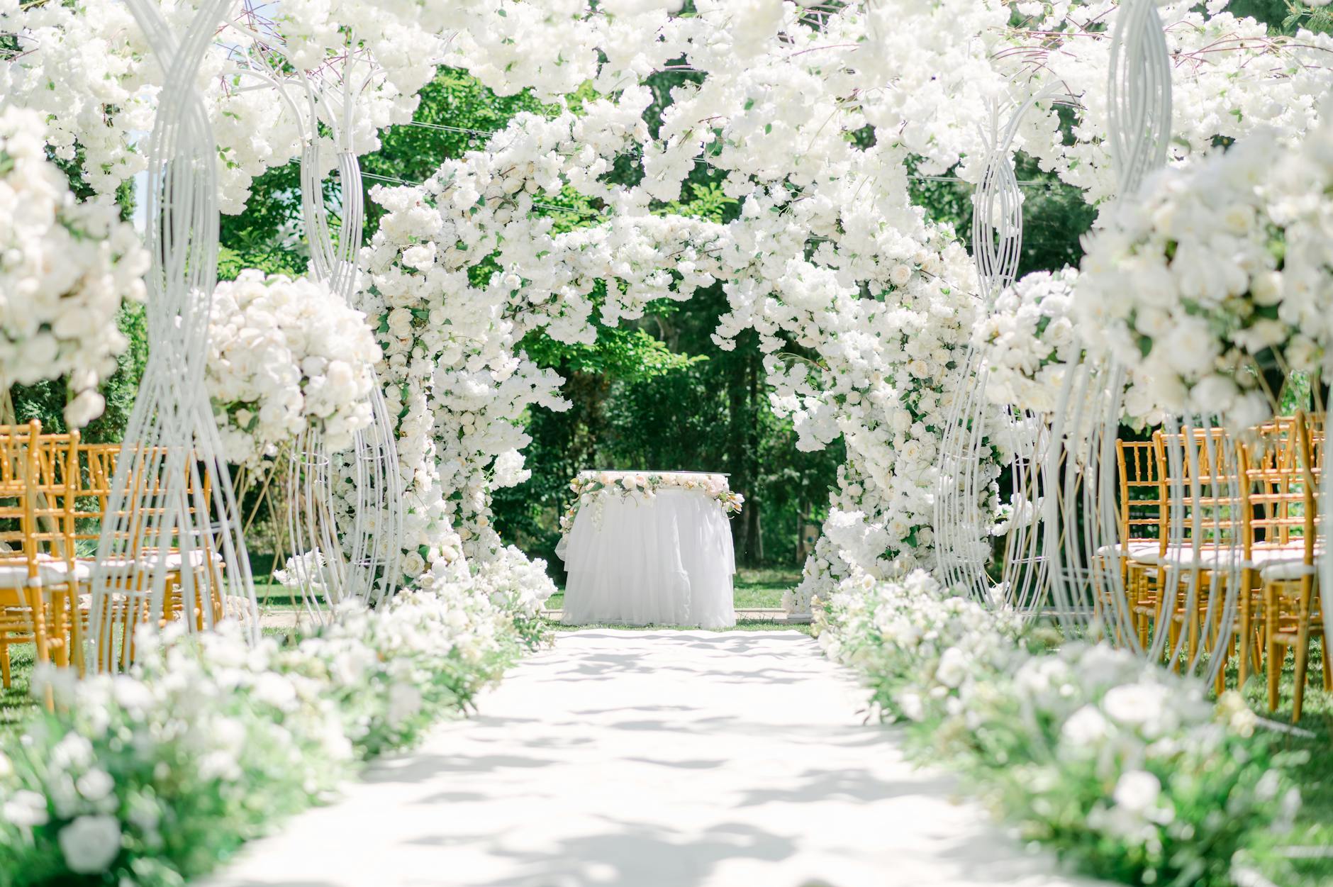 An elegant outdoor wedding venue setup with white floral arches and chairs. - wedding planning stress