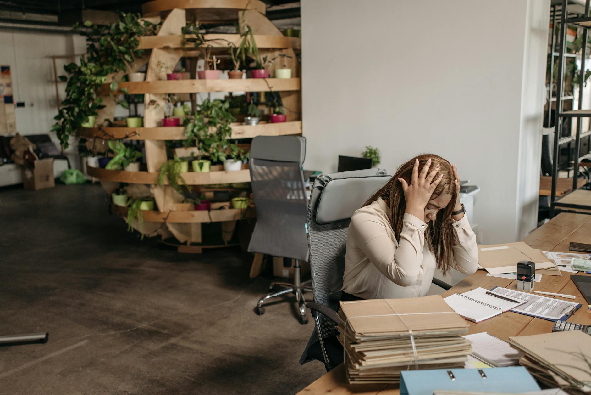 A stressed woman sits overwhelmed at her desk, surrounded by paperwork in a modern office setting. - wedding planning stress